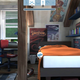 The new poster, to the left of the bed’s headboard, replaces the nudity-laden demon poster that caused the game to get pulled.